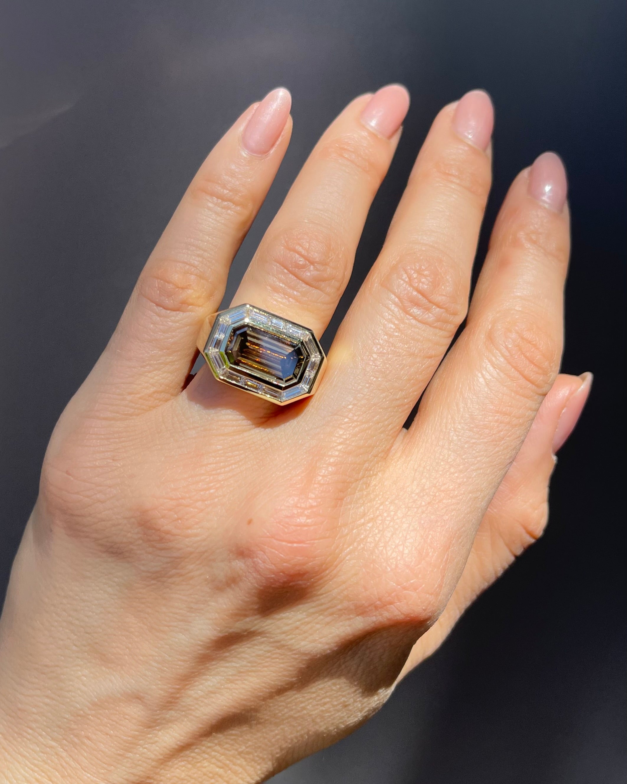 Hand wearing a ring with a large gemstone on a dark background